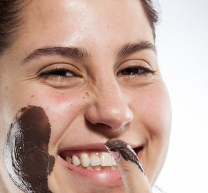 Smiling woman applying Sundae Best® Chocolate Softening Mask with CoQ10 | Farmhouse Fresh on her cheek, showcasing smooth skincare and a joyful moment of self-care.