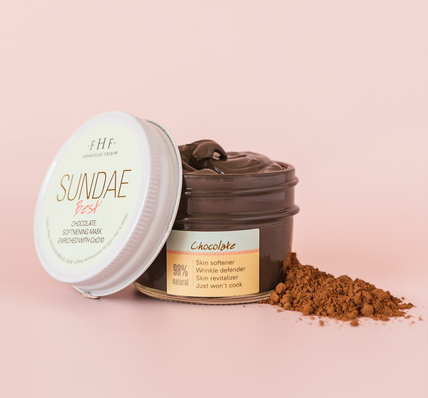 Open jar of Sundae Best® Chocolate Softening Mask with CoQ10 | Farmhouse Fresh showing rich chocolate-colored cream next to a pile of cocoa powder on a soft pink background.