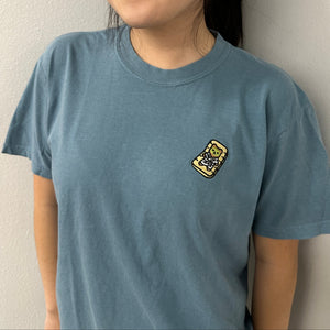 Person wearing a soft blue comfortable t-shirt featuring a small embroidered lounging bear design on the chest, showcasing the Lounging Spa Bear Comfy Tee | Lucky Owl.