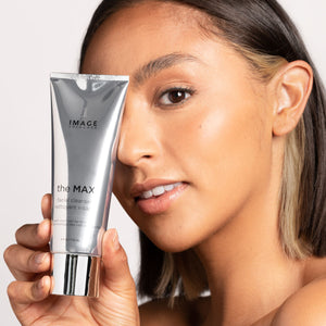 Close-up of a woman holding the MAX™ facial cleanser | IMAGE Skincare, showcasing clear, healthy skin and the sleek silver packaging of the skincare product.