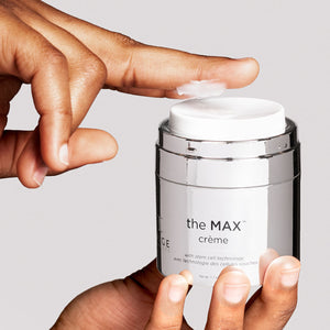 Close-up of a hand holding the MAX™ crème | IMAGE Skincare jar while applying a small amount of cream on the fingertip, highlighting skincare and wellness.
