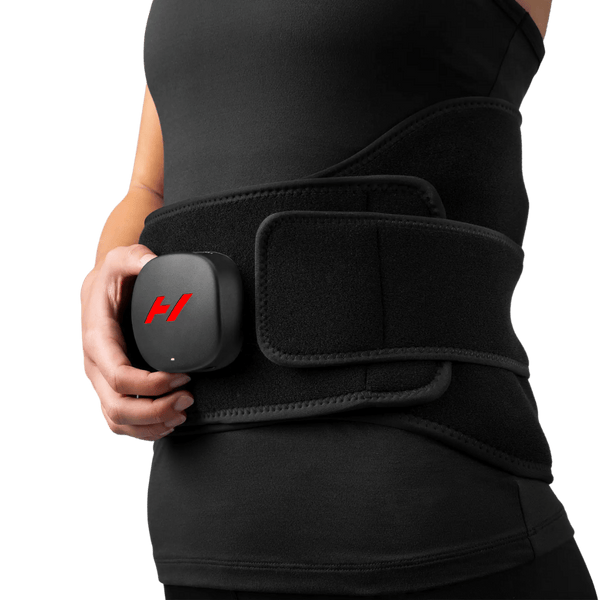Person wearing the Venom 2 Back | Hyperice black wearable recovery device around their lower back, holding the compact control unit attached to the belt.