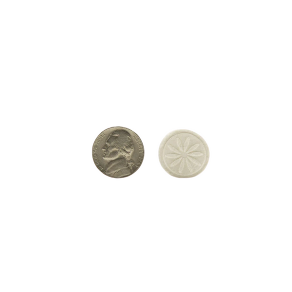 A close-up of a round, white skincare tablet embossed with a flower design next to a nickel for size comparison, related to Essential Wipes Plus - Eco Pak (35 wipes) | Functional Botanicals.