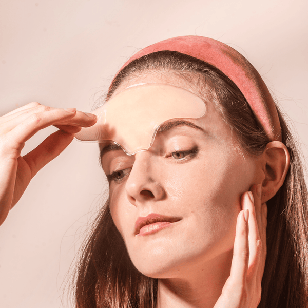 Woman applying a transparent Skin Plumping Reusable Forehead Pad | Dreambox Beauty to her forehead, demonstrating a skincare routine for smooth and hydrated skin.