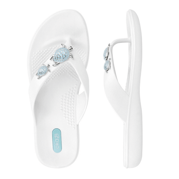 White flip-flop sandals with blue and silver turtle embellishments on the straps, featuring textured footbeds for comfort, named Theresa | Oka-B.