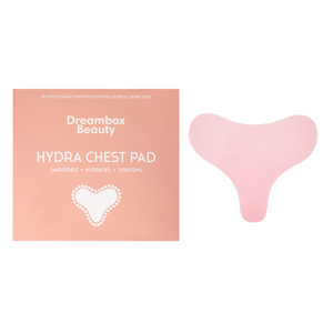 Pink hydrating reusable chest pad with smooth curved design displayed next to peach-colored packaging labeled Dreambox Beauty Hydra Chest Pad promoting skin smoothing, hydration, and tightening benefits, featuring the product title Hydrating Reusable Chest Pad | Dreambox Beauty for wellness and skincare.