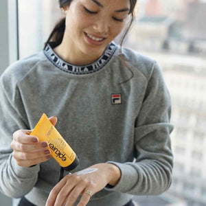 Woman wearing a gray sweatshirt applying Zinc Oxide Perfecting Sunscreen | Epicuren Discovery on her hand, demonstrating skincare and sun protection.