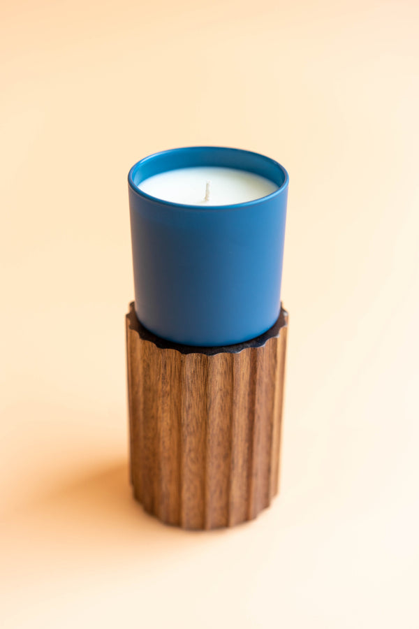 Oakmoss + Amber Dignity Series Glass Jar Soy Candle | Calyan Wax Co. - 5.3 oz in a matte blue glass container placed on a textured wooden holder against a soft beige background