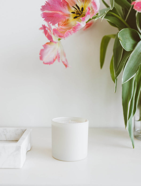 White glass jar candle on a white surface next to a marble tray with a pink and white tulip overhead, Aspen + Fog Dignity Series Glass Jar Soy Candle | Calyan Wax Co. - 5.3 oz