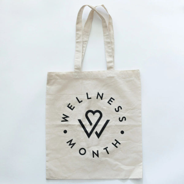 Natural cotton tote bag with black Wellness Month logo and heart design, promoting wellness and self-care, named Wellness Month Tote Bag | Wellness Month.