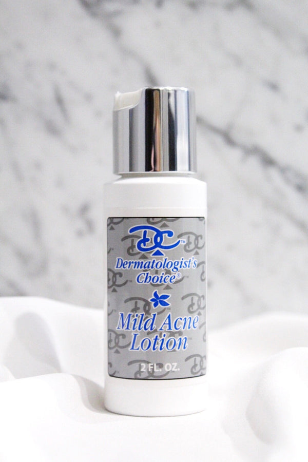 Bottle of Mild Acne Lotion with Benzoyl Peroxide | Dermatologist's Choice standing on a white fabric surface with a marble background, featuring skincare product packaging.