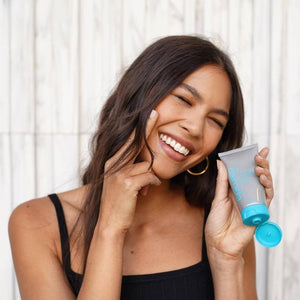 Smiling woman with clear skin holding a tube of Acidophilus Probiotic Facial Cream | Epicuren Discovery, promoting skincare and wellness in a natural light setting.